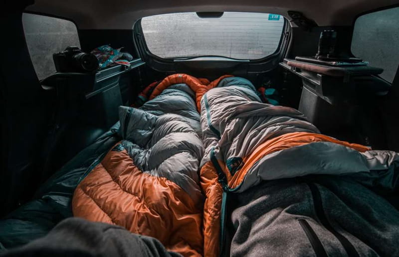 A person sleeping comfortably in the back of an SUV with pillows and a blanket.